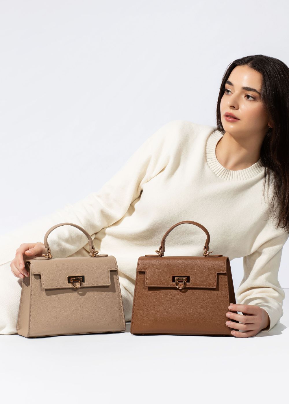 Model in white outfit hold two top handle bags in brown and taupe from layla collection by Levantine