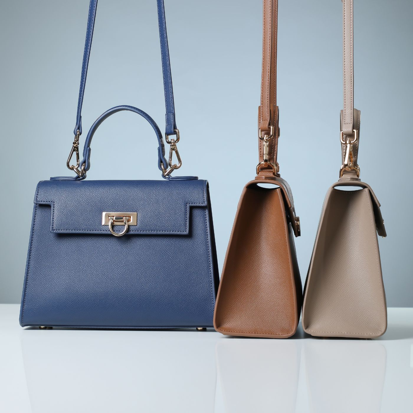 Three layla top handle handbags of different colors, navy blue, Brown and taupe can be woren as a satchel or a crossbody bag