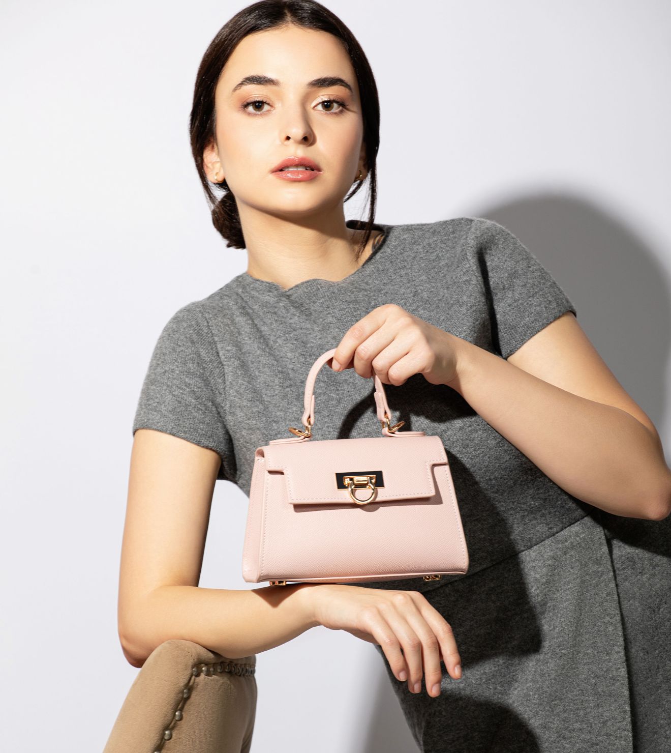 Model in a chic gray dress holds a stylish pink purse By levantine bags, epitomizing luxury and grace