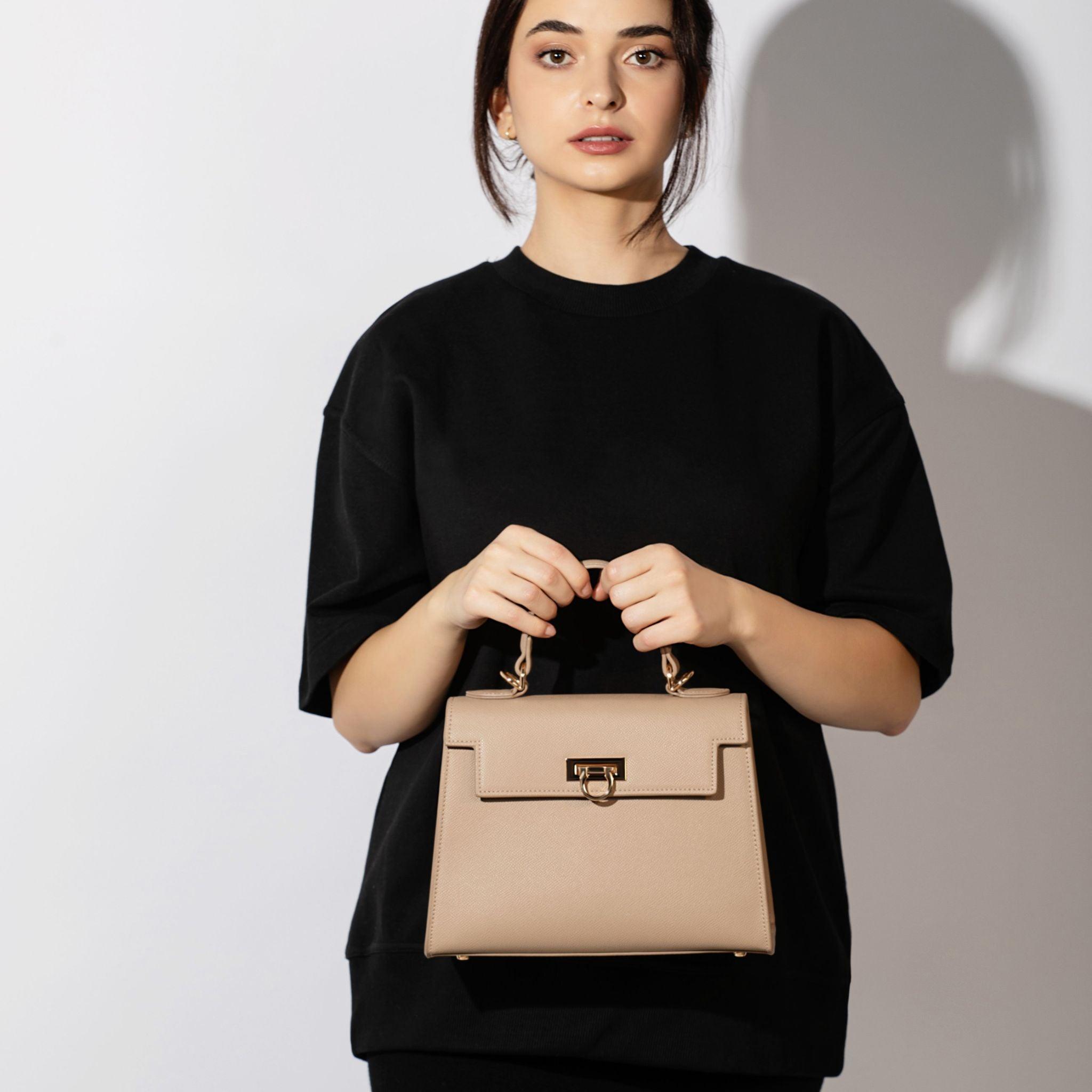 Elegant woman holding a chic taupe handbag.